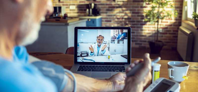 Man taking blood pressure while speaking with doctor at telehealth appointment
