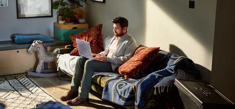 Person sitting on couch in living room and using laptop.