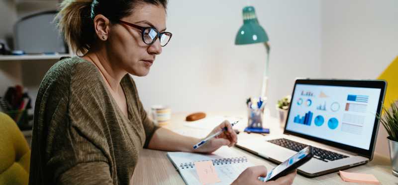 Person sitting at a computer reviewing financials and looking at a phone.