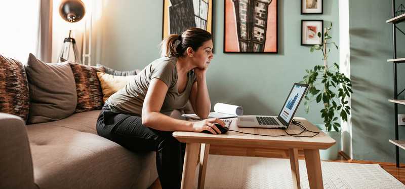 Person leaning to use laptop computer on coffee table in living room.