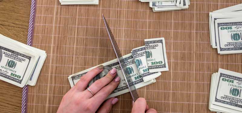 Person cutting dollars into pieces with a knife.