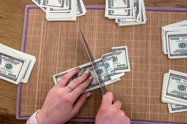 Person cutting dollars into pieces with a knife.