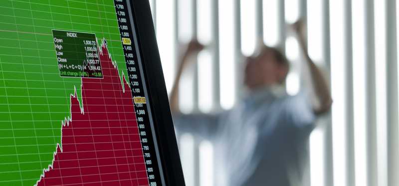 Market crash on screen in foreground with upset person in background.