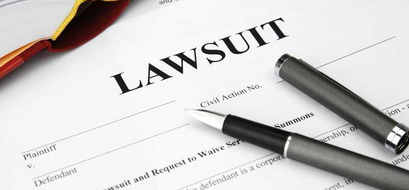 Paperwork reading Lawsuit with pens on top