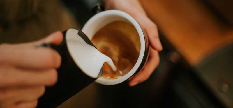 Barista pouring milk in coffee to make latte