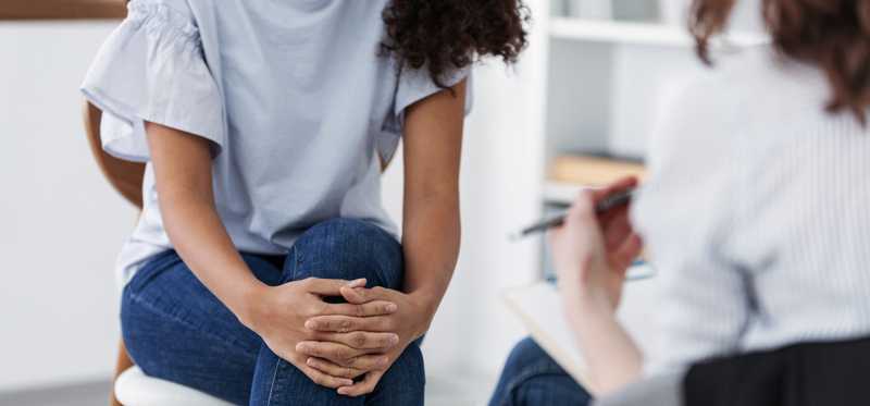 Woman in gray shirt and jeans sitting talking to doctor