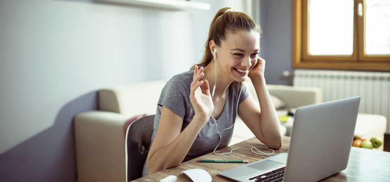 Woman sitting at laptop smiling and chatting with coworkers through video conference