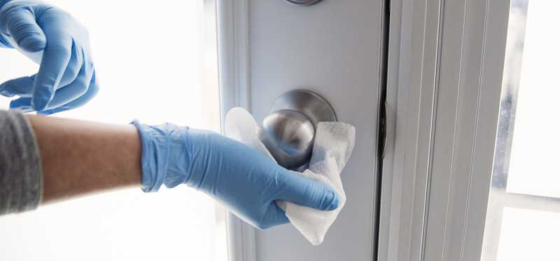 Person wearing blue latex gloves and cleaning doorknob with wipe.