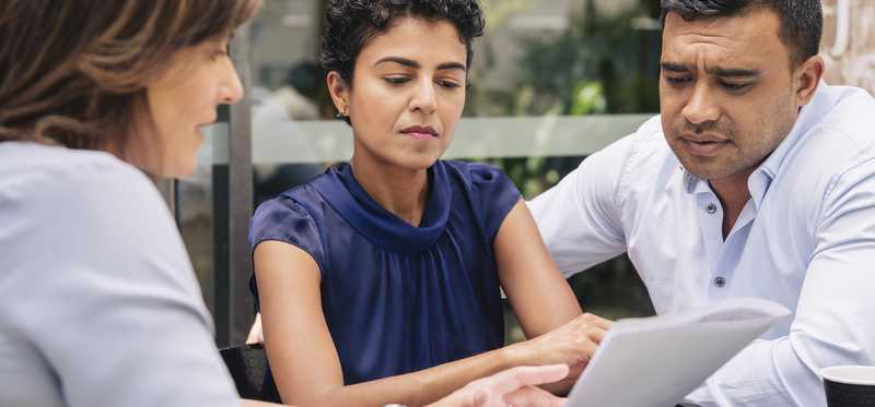 Three people reviewing paperwork outside.