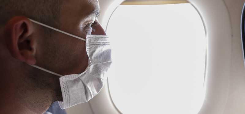 Masked man looking out airplane window