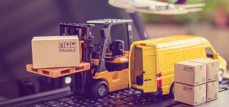 Miniature yellow van, boxes, and pallet truck on top of black laptop