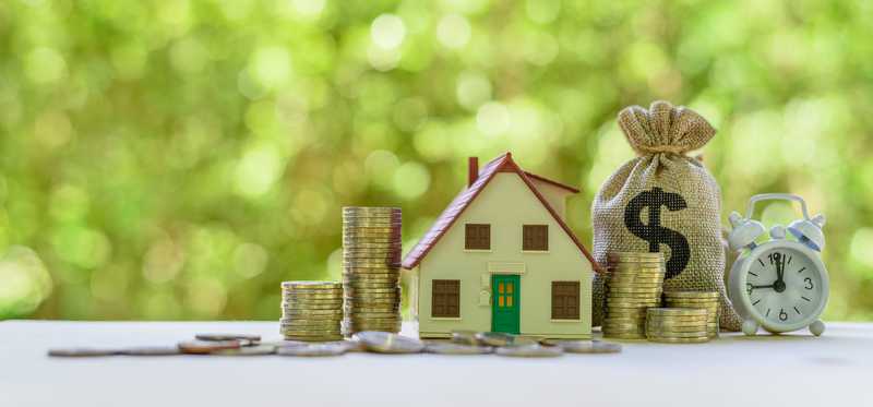 Model of house next to a bag of money with a dollar sign on it and stacks of gold coins.