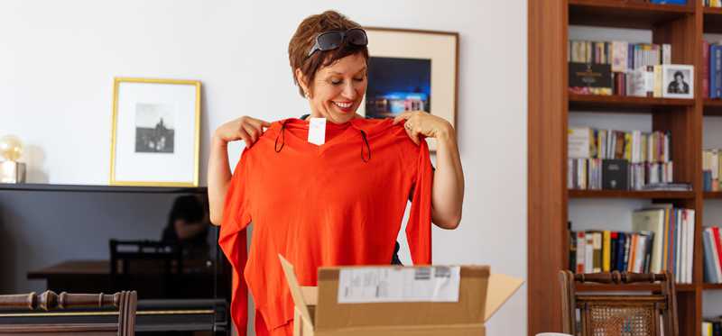 Woman holding sweater that she just received in the mail and smiling