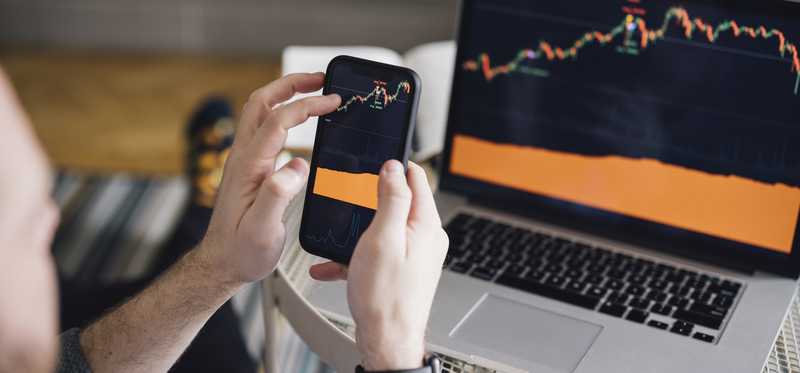 Person holding a phone showing same stock market chart as laptop.