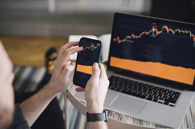 Person holding a phone showing same stock market chart as laptop.