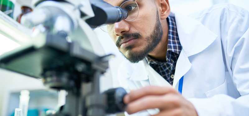 Man in white labcoat looking through microscope.