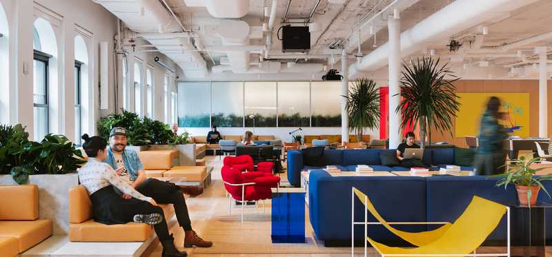 Two people sit inside the lobby of a trendy office.
