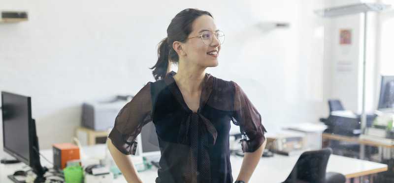 Businessperson standing in office while smiling and looking into the distance.