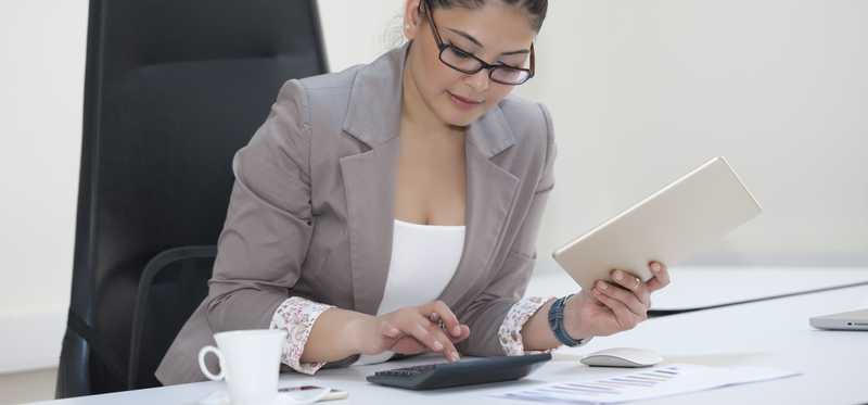 Businesswoman sitting at desk reviewing paperwork and using calculator