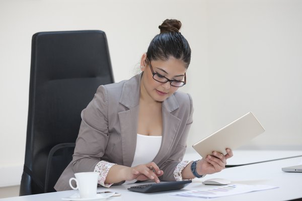 Businesswoman sitting at desk reviewing paperwork and using calculator