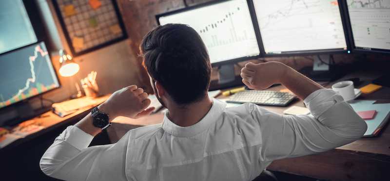 Investor stretching while sitting in front of computer screens