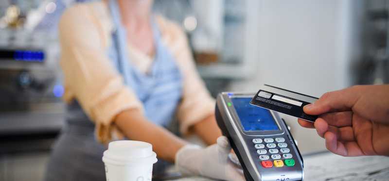 Person purchasing coffee from masked barista with credit card