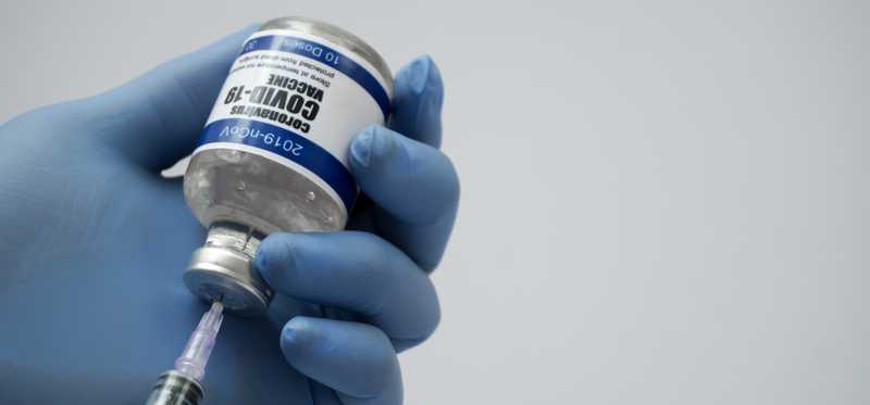 Worker in blue latex gloves dispensing dose of COVID-19 vaccine through syringe.
