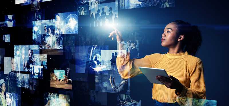 Woman in yellow sweater holding tablet and flipping through various screen projections
