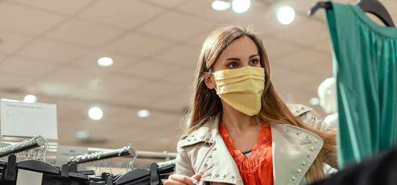 Woman with trench coat and mask shopping for clothes