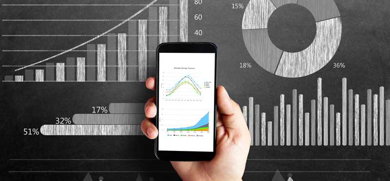 Phone being held in front of charts and graphs.