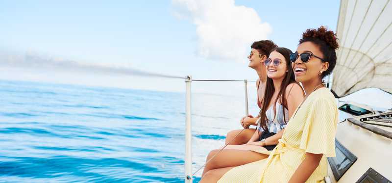 Three people smile while sitting on the side of a boat.