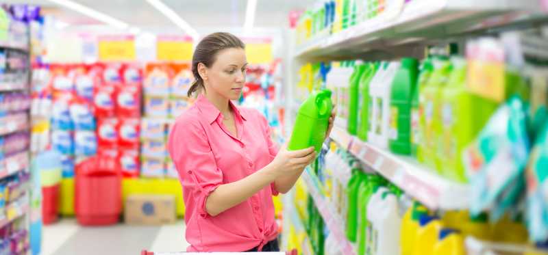 Person holding and looking at laundry detergent while shopping in supermarket.