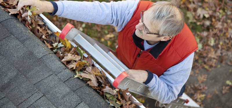 Man on a ladder cleaning gutters.