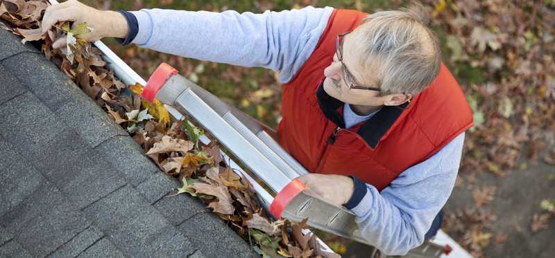 Person on a ladder cleaning gutters.