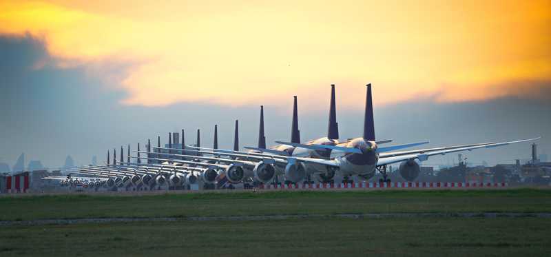 Airplanes parked in a row on tarmac against sunset backdrop