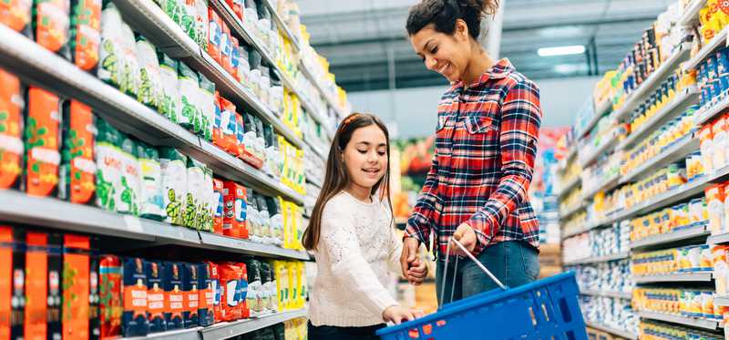Mother and daughter browsing grocery aisle and placing items in blue shopping basket