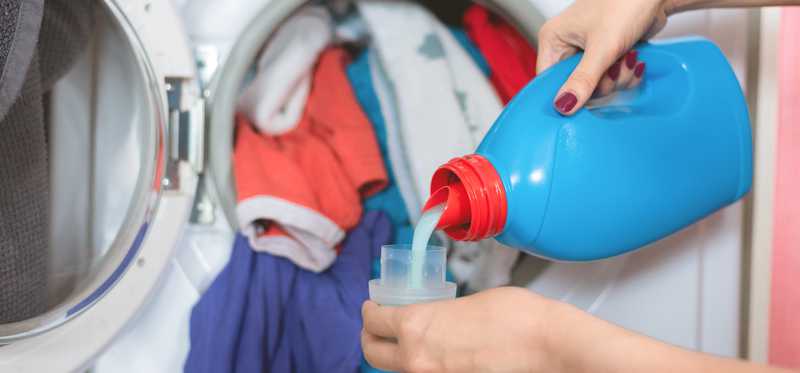 Person pouring laundry soap into lid with load of laundry in background