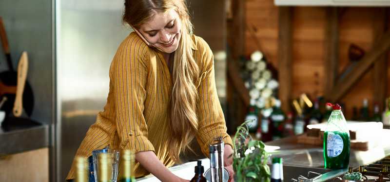 Smiling woman talking on the phone while washing dishes at kitchen sink