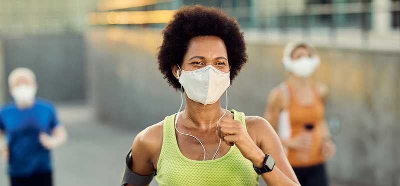 Woman in green tank top wearing face mask while going for a run