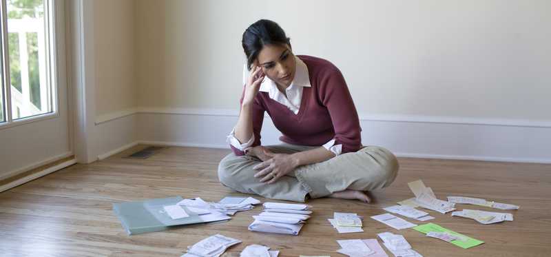 Person sitting on floor looks thoughtful while surrounded by piles of paperwork.