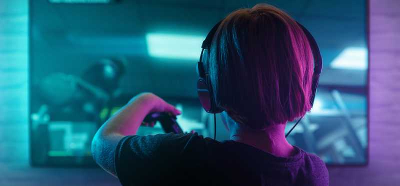 Person wearing headphones, holding game console, and playing video games.