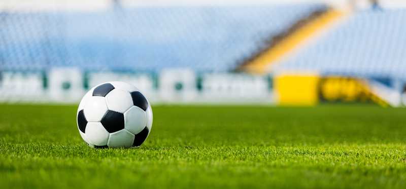 Soccer ball on field with advertising posters blurred out on stadium walls in background.