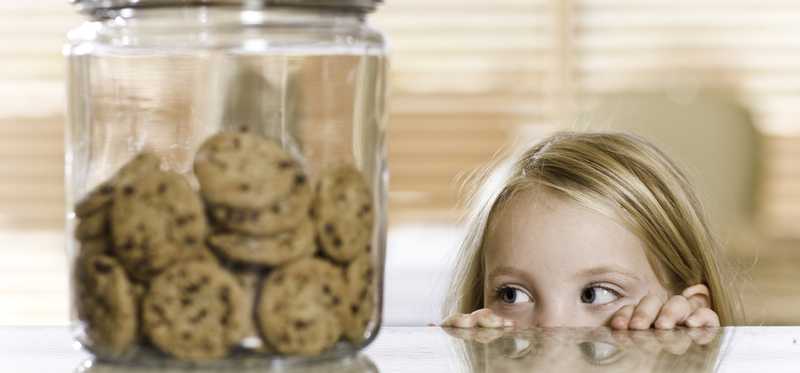 Child peers over counter to look at cookie jar.