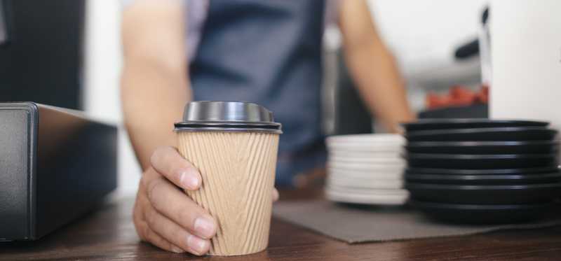 Barista placing paper coffee cup on shop counter