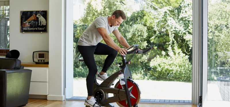 Man riding exercise bike at home near large window looking out on backyard