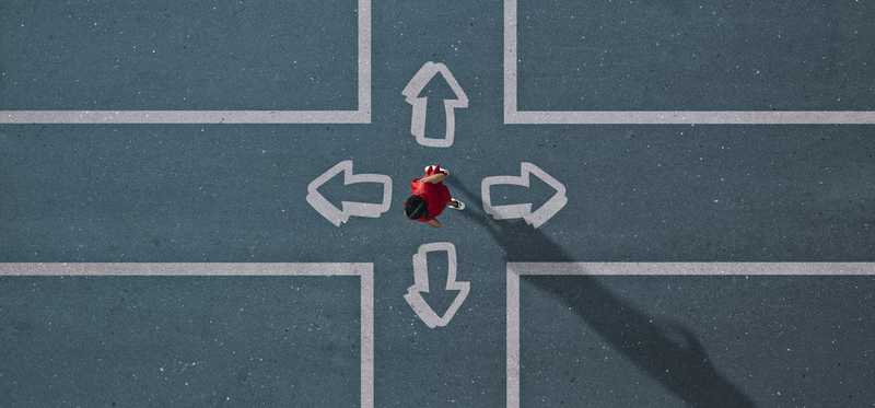 Person standing at crossroads intersection with arrows pointing in all directions