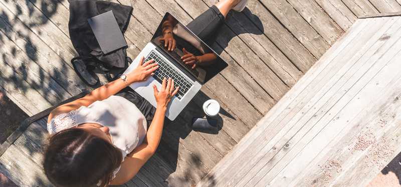 Person working on a laptop on a sunny deck.