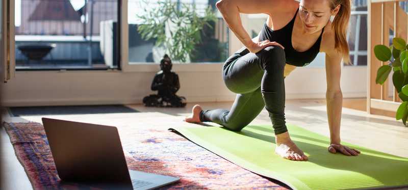 Woman doing yoga at in sunny living room and watching tutorial on laptop