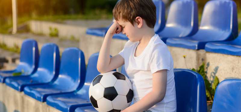 Boy sitting in stadium with soccer ball on his lab and fist to his head.