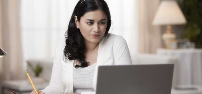 Person at desk is looking at laptop and writing notes.